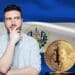 Hombre pensativo junto a un bitcoin y la bandera de El Salvador.