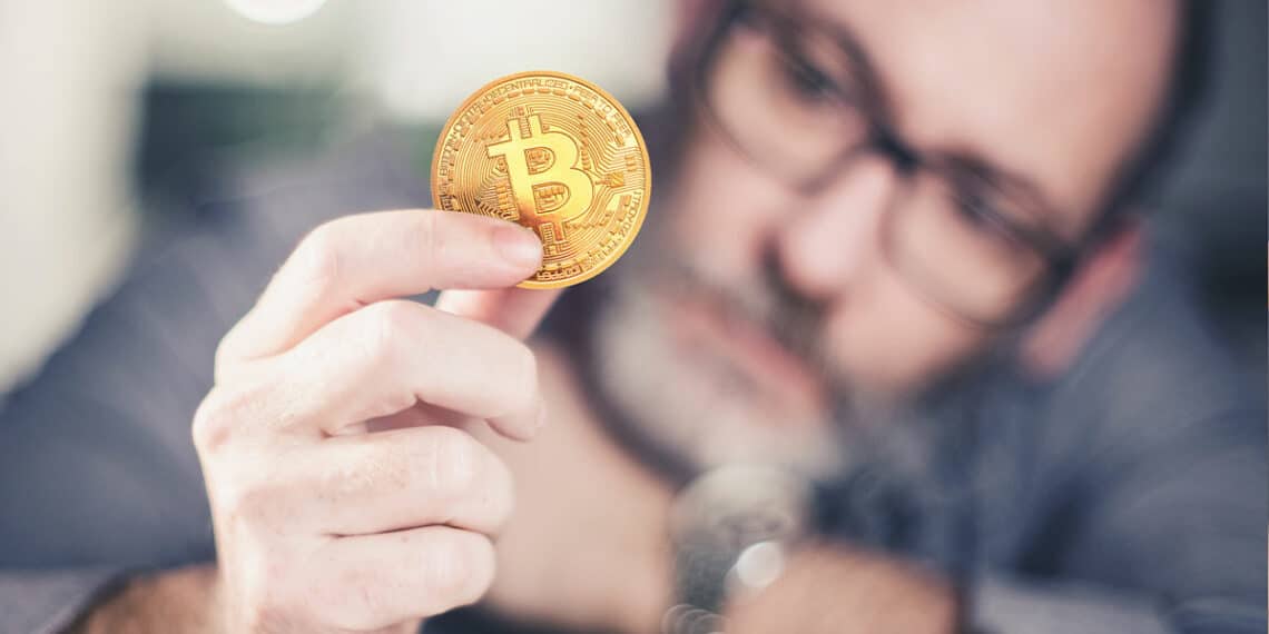 hombre sostiene moneda de bitcoin mientras la evalua