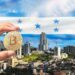 mano sostiene moneda de bitcoin en frente de ciudad con bandera de Honduras en el fondo