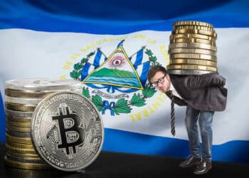 hombre sostiene pila de monedas junto a moneda de bitocin con bandera de El Salvador en el fondo