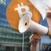 hombre protestando con logo de bitcoin y oficinas de la SEC en el fondo