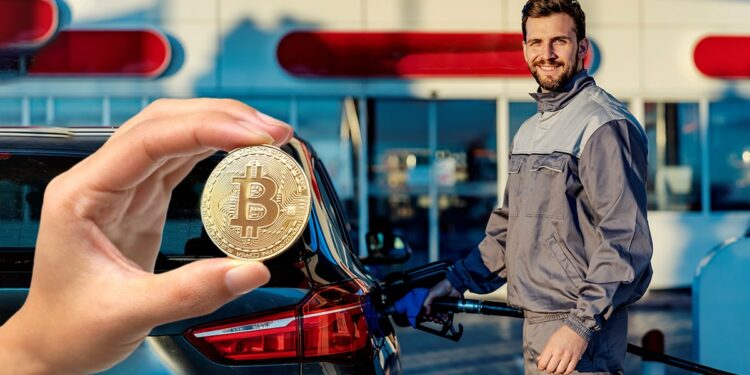 Mano muestra moneda de bitcoin con hombre cargando gasolina a su automovil en el fondo