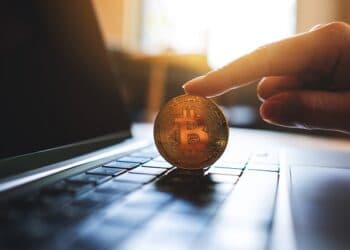 persona sostiene moneda de bitcoin sobre computadora
