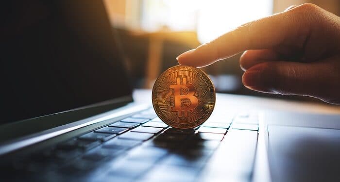 persona sostiene moneda de bitcoin sobre computadora