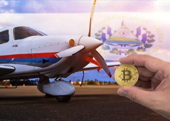 mano sosteniendo moneda de bitcoin con avioneta estacionada y bandera de El Salvador en el fondo