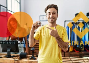 Joven sosteniendo moneda de bitcoin en tienda de ropa con logos de Binance y Mastercard en el fondo