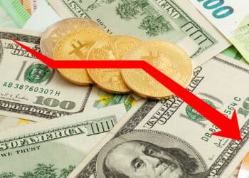 flecha bajista sobre monedas de bitcoin sobre billetes de euro y dolares