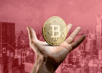 mano sostiene moneda de bitcoin con ciudad en rojo en el fondo