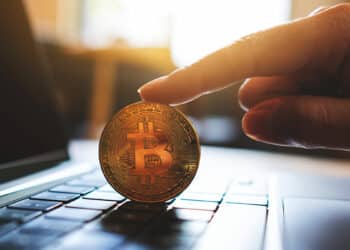 Bitcoin sobre laptop sostenido por mano