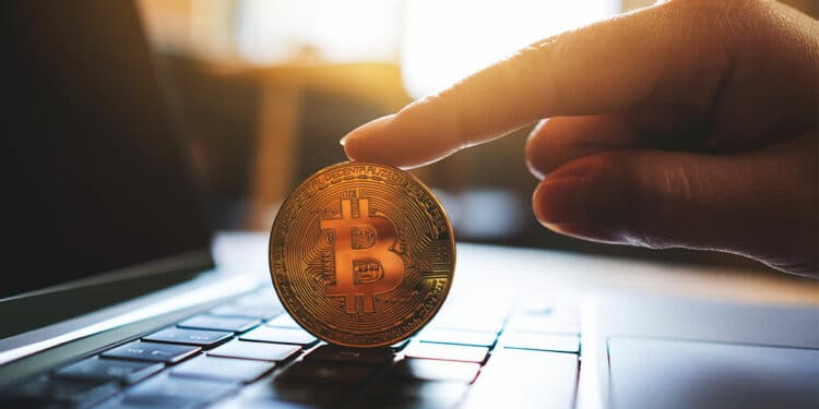 Bitcoin sobre laptop sostenido por mano