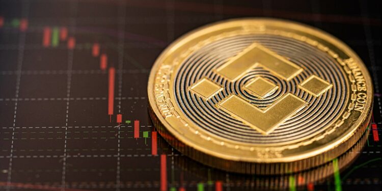 moneda de Binance sobre superficie con gráfico de precio descendiendo