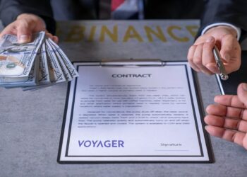 hombre de negocios ofrece dinero, boligrafo y documento con logo de Voyager con logo de binance sobre mesa