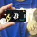 mano sostiene tarjeta bold con bitcoins sobre bandera de El Salvador en el fondo