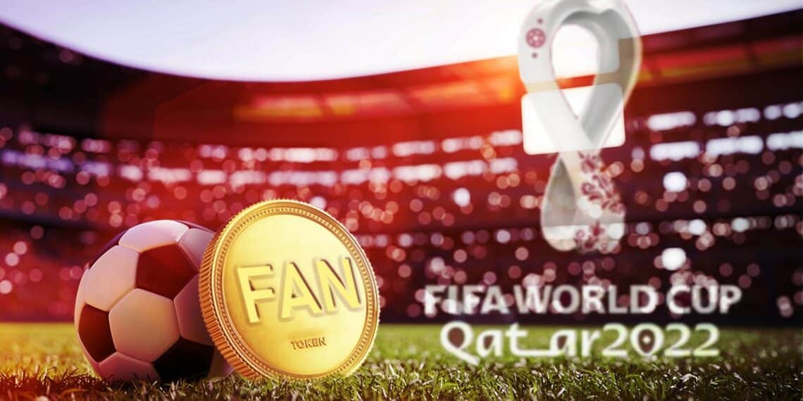 moneda de fan token apoyada en balón de futbol en campo de juego con logo del mundial de futbol en Quatar 2022