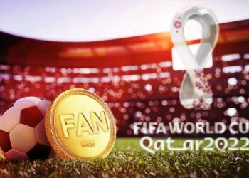 moneda de fan token apoyada en balón de futbol en campo de juego con logo del mundial de futbol en Quatar 2022