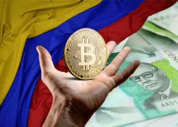 Pesos y bandera colombiana con mano sosteniendo btc