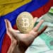 Pesos y bandera colombiana con mano sosteniendo btc