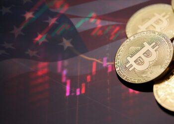 monedas de bitcoin sobre mesa con bandera de Estados unidos y rgáfico de inflación reflejados