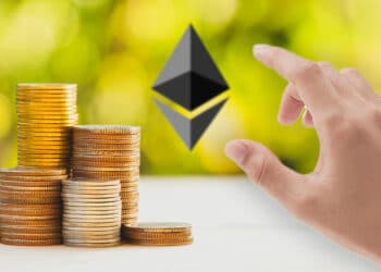 Pila de monedas con logo de ETh al fondo y mano