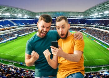 hombres celebrando con telefono en mano en estadio de futbol