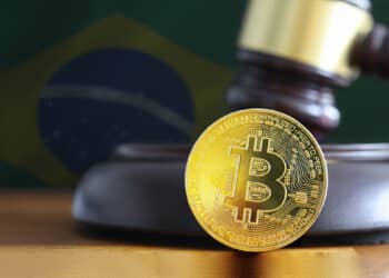 moneda de bitcoin sobre mesa en frente de martilllo de juez con bandera de brasil en el fondo