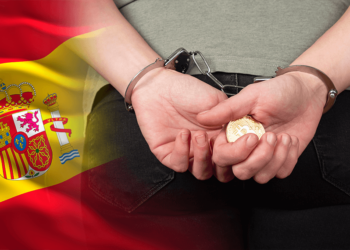 Bandera de España junto a persona arrestada con un bitcoin en la mano.