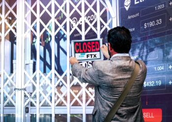 hombre colgando letrero de cerrado en tienda con graficos de mercado y logo de ftx