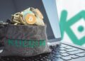 bolsa con logo de kucoin llena de criptomonedas sobre computadora con loo de kucoin en el fondo