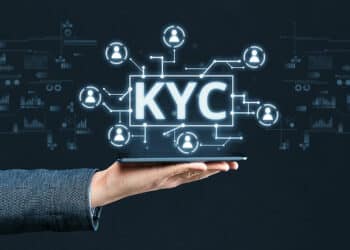 Mano de persona sosteniendo teléfono con gráficos y siglas KYC