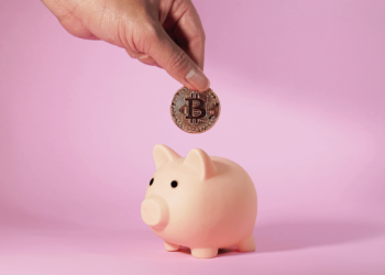 mano depositando monedad de bitcoin en alcancía de cochinito.