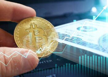 mano sosteniendo moneda de bitcoin entre sus dedos junto a billetes de dólares apilados con gráficos indicando aumento superpuestos