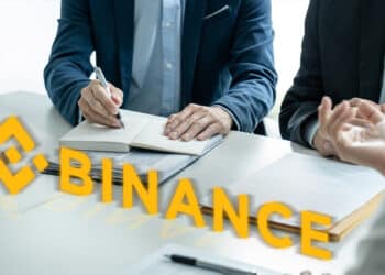 Logo de Binance en mesa con personas, documentos y maso de juez llegando a un acuerdo