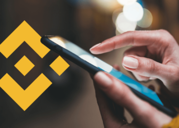 persona usando teléfono móvil con logo de Binance en el fondo