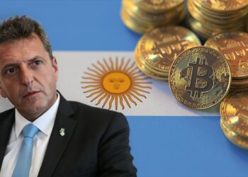 Sergio Massa junto a monedas de bitcoin apiladas sobre bandera de Argentina