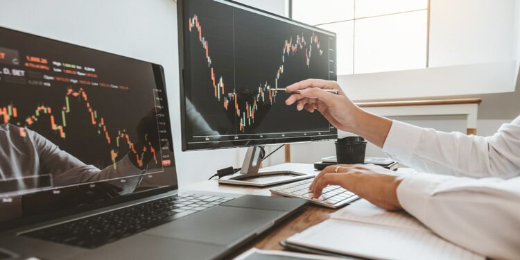 trader señala gráfico de precio en pantallas de computadora
