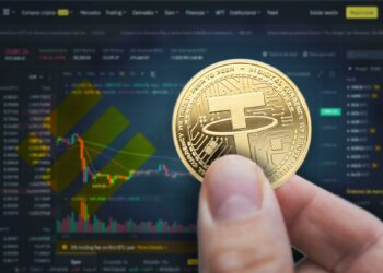 mano sosteniendo moneda de tether con plataforma del exchange binance y logo de la syablecoin BUSD en el fondo
