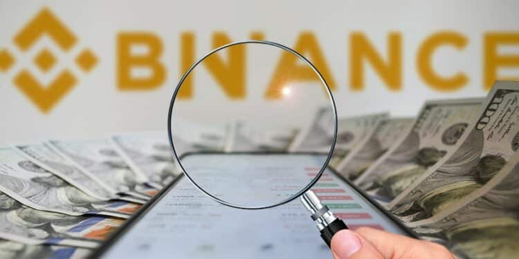 mano sosteniendo lupa sobre teléfono sobre billetes de dólares con logo de Binance en el fondo