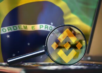 Lupa con logo de Binance sobre computadora con bandera de Brasil en el fondo