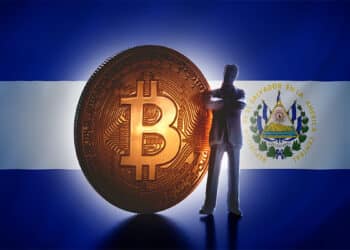 Hombre de negocios parado junto a moneda de bitcoin con bandera de El Salvador en el fondo