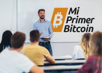 profesor dando clase a jovenes adultos con logo de Mi Primer Bitcoin en la pizarra