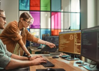 programadores trabajando código en computadora con logo de bitcoin en pantalla