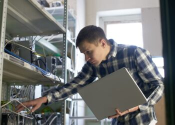 hombre revisando equipos ASIC para la minería de bitcoin en estántes dentro de su hogar