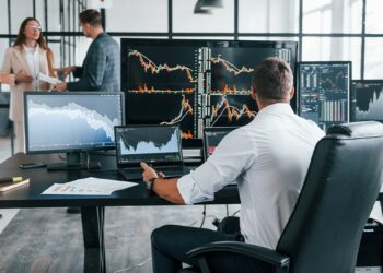 trader ssentado en escritorio siguiendo graficos de precios en diversas pantallas