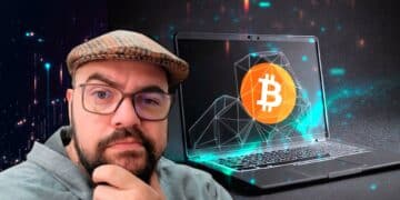 David Battaglia junto con una computadora que muestra un logo de bitcoin.