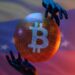 manos sosteniendo globo con logo de Bitcoin y bandera de Venezuela en el fondo