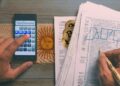 persona calculando impuestos y llenando formularios con logo de la AFIP con monedas de bitcoin escondidas entre hojas y bandera de argentina pintada sobre la mesa