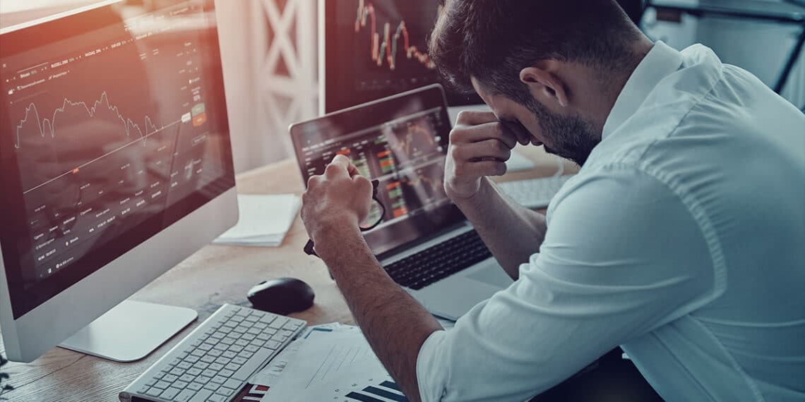 trader cansado sentado en escritorio con grafico de precio bajista en pantalla de computadora