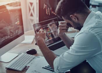 trader cansado sentado en escritorio con grafico de precio bajista en pantalla de computadora