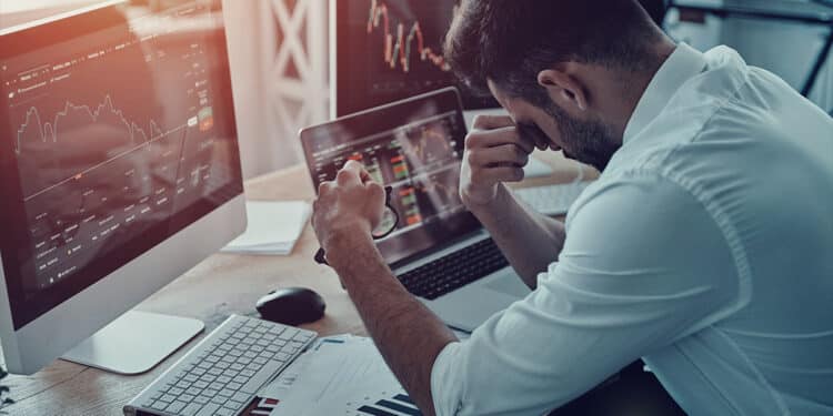 trader cansado sentado en escritorio con grafico de precio bajista en pantalla de computadora