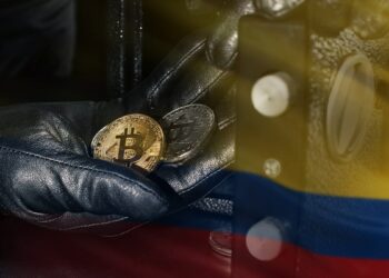 manos de ladron retirando monedas de bitcoin de caja fuerte con bandera de Colombia superpuesta